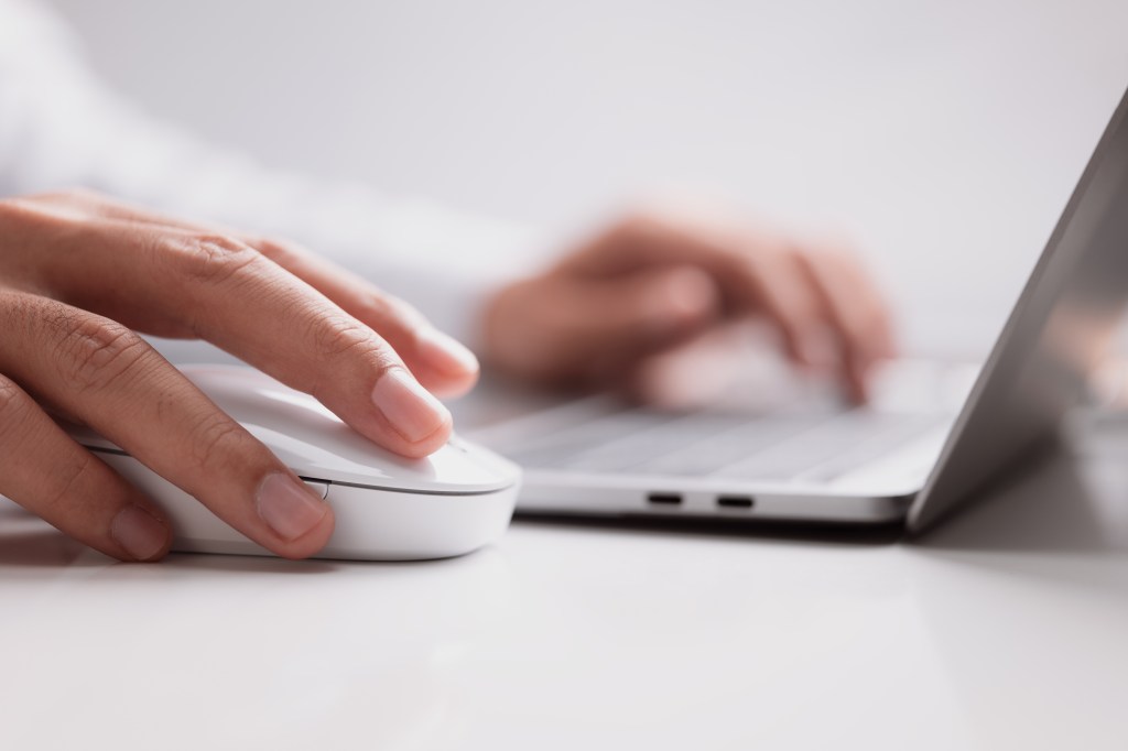 Male hand holds a computer mouse and typing laptop keyboard.